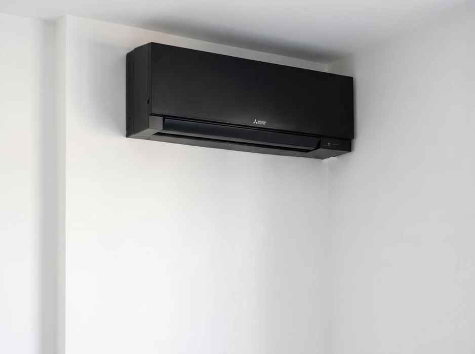 Unité intérieure de climatisation split-system Mitsubishi Electric, coloris noir mat, montée en applique murale dans un angle de pièce aux murs blancs