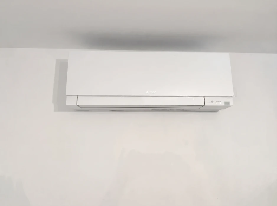 Unité intérieure de climatisation murale **Mitsubishi Electric**, modèle split system, montée en hauteur sur mur blanc