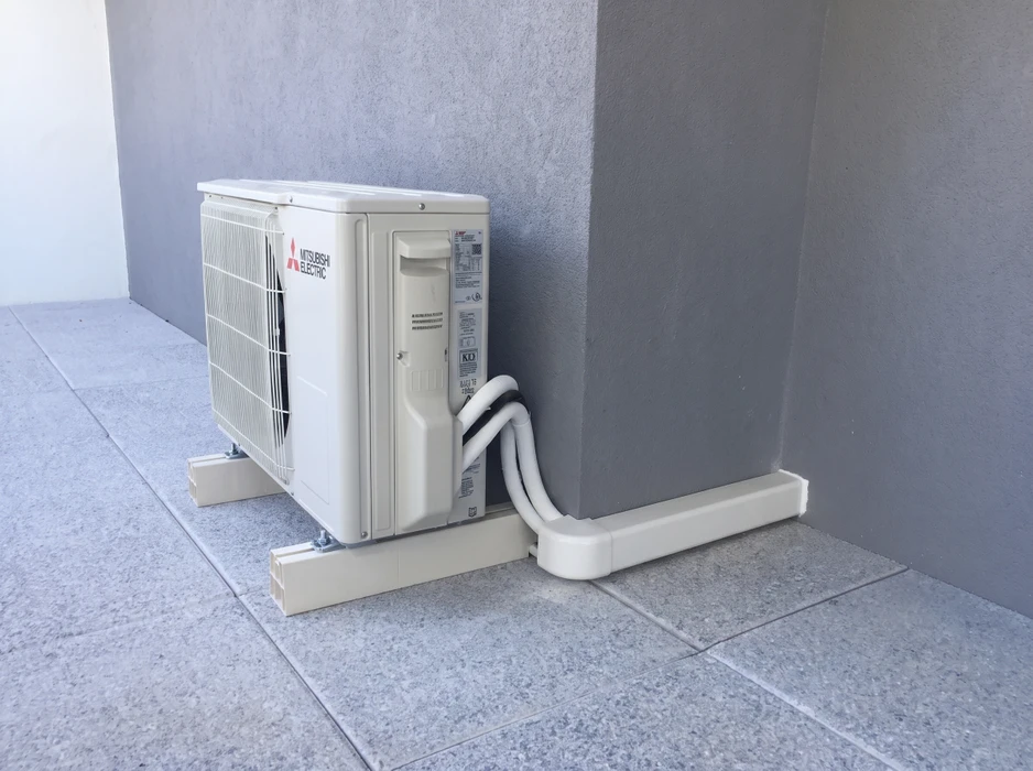 Unité extérieure de climatisation split Mitsubishi Electric installée en angle de mur extérieur, posée sur patins antivibratoires