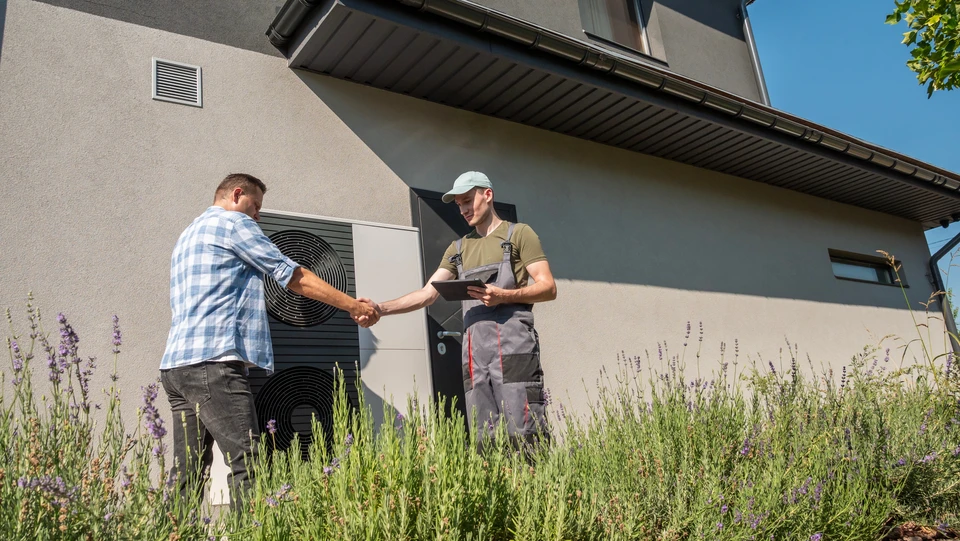 Photographie d'un technicien climat ou du responsable de Thermo-Logis souriant et bienveillant, discutant face à face avec un client dans l'intérieur résidentiel de celui-ci, à proximité d'une unité Mitsubishi Electric installée. L'atmosphère doit transmettre la confiance, la disponibilité et l'écoute attentive. Éviter les poses figées ou génériques : privilégier un moment authentique de dialogue professionnel et courtois reflétant la relation de proximité et la personnalisation du service.