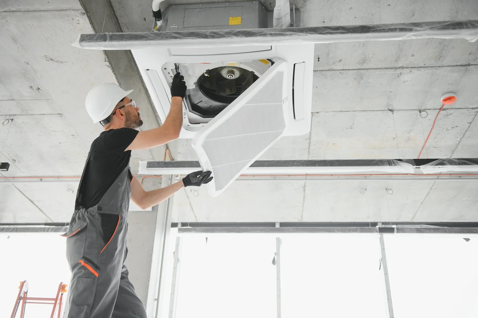 Unité extérieure de climatisation blanche installée contre un mur beige, positionnée sur un sol carrelé clair