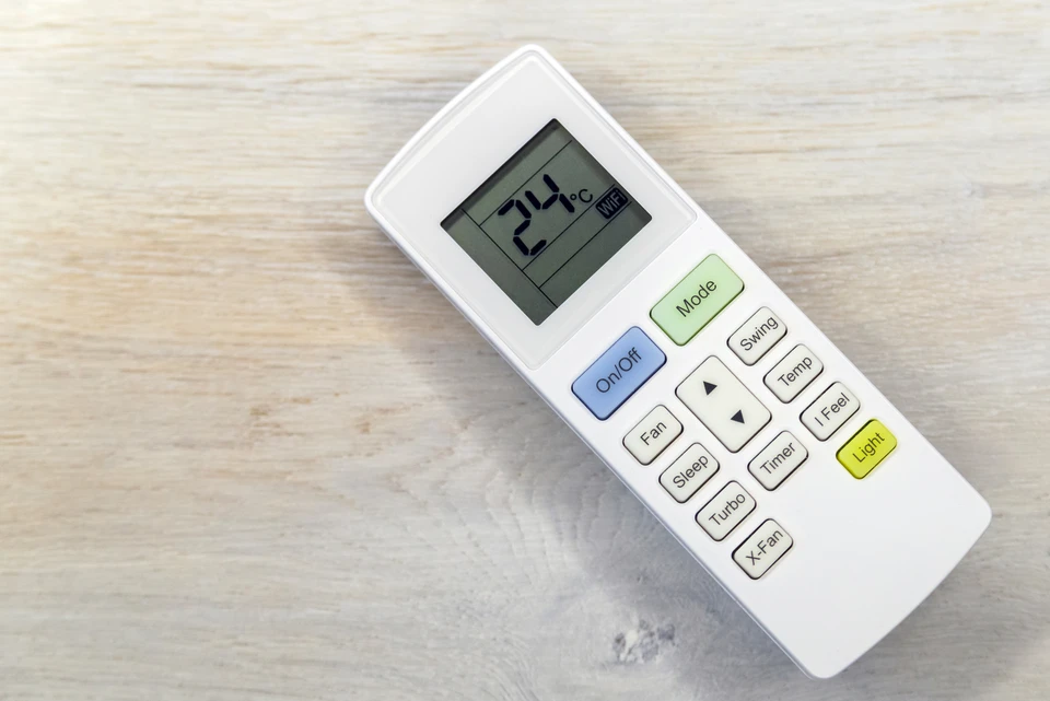 Intérieur résidentiel avec main tenant télécommande de climatiseur pointée vers unité murale blanche