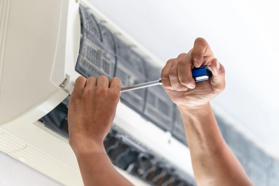 Technicien en uniforme blanc effectuant la maintenance d'un climatiseur mural split dans un intérieur résidentiel moderne aux murs blancs avec rideaux gris