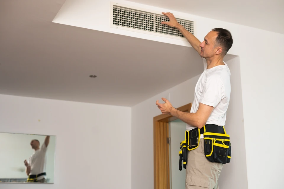 Photo réelle d'une installation de climatisation réversible Mitsubishi Electric en cours de réalisation, montrant un technicien vêtu d'une tenue de travail professionnelle effectuant les raccordements frigorifiques d'une unité extérieure avec des outils appropriés. L'unité extérieure est installée sur patins antivibratoires, avec les gaines et conduites soigneusement organisées en plinthe. Arrière-plan : façade résidentielle claire. La scène doit exprimer la rigueur technique, l'attention aux détails et le professionnalisme d'une installation haut de gamme.